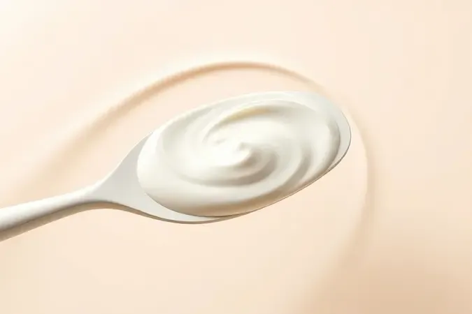 Aplicação conceitual de creme hidratante perolado sendo espalhado suavemente sobre superfície curva e limpa.